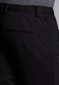 Svarta byxor med en texturerad midja, en enskild bakficka med en subtil fäll, och en slät tygfinish.