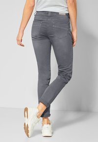 Jeans ajustados grises con una textura suave, detalles de costura sutil, puños enrollados y dos bolsillos traseros. Combinados con zapatillas blancas.