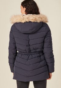 Chaqueta de plumas azul marino con capucha de piel sintética, textura acolchada, cinturilla ajustable y puños elásticos, diseñada para brindar calidez y comodidad.