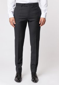 Dunkelgraue maßgeschneiderte Hose mit glatter Textur, ausgestattet mit einem Knopfverschluss, vorderen Nähten und slim fit Design. Kombiniert mit schwarzen Schuhen.