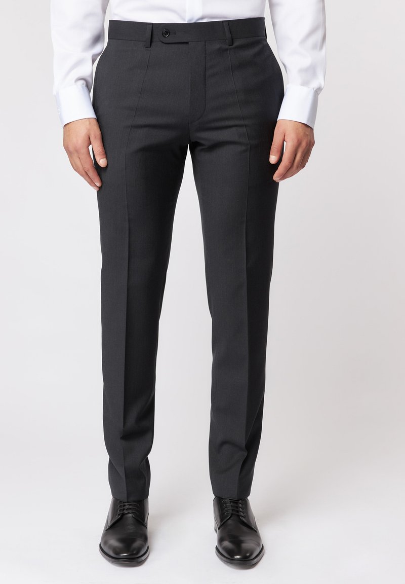 Dunkelgraue maßgeschneiderte Hose mit glatter Textur, ausgestattet mit einem Knopfverschluss, vorderen Nähten und slim fit Design. Kombiniert mit schwarzen Schuhen.