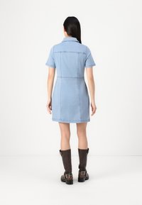 Džínová košilová šaty, svetlomodrá, krátke rukávy, s golierom, priliehavý pás, výstrih na chrbte, nadkolenová dĺžka, v kombinácii s hnedými čižmami po kolená.