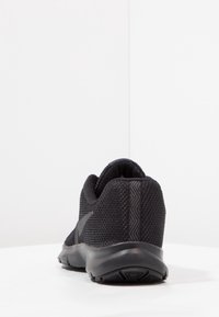 Black athletic shoe with a textured mesh upper, curved heel, and flexible rubber sole. Features minimal branding and a padded collar for comfort.