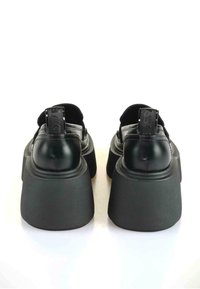 Melni platformas zābaki ar gludu ādas virsu, teksturētu gumijas zoli un redzamu cilpu aizmugurē, kas atvieglo uzvilkšanu.