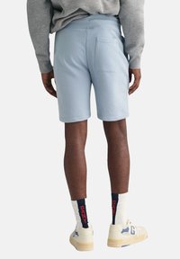 Shorts bleu clair en tissu doux, dotés d'une poche arrière et d'une taille élastique, associés à des chaussettes blanches et des baskets beiges.