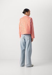 Jacket matlasat în dungi portocalii și albe, cu un croi drept și un guler ribbed, asortat cu blugi din denim lejeri, de culoare albastră deschisă, cu picioare largi.