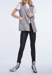 Grå rutig ärmlös blazer med två framfickor, ihopparad med en vit t-shirt med grafik och svarta läderliknande byxor. Snakeskins-präglade ankelstövlar.