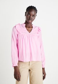 Blusa a maniche lunghe di un rosa chiaro con scollatura voluminosa e corpino arricciato, con polsini elastici e una vestibilità comoda.