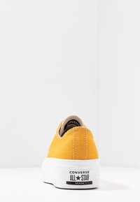 Keltainen kanvaslenkkari valkoisella kumipohjalla. Siinä on takalokografiikka ja ompeluyksityiskohtia. Pyöreä kärkimuotoilu, alhainen malli.