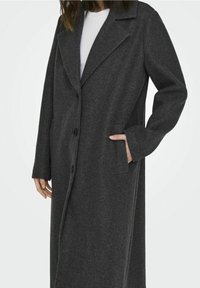 Abrigo largo de lana gris oscuro con cuello con muesca, cierre de botones y bolsillos laterales. Presenta un corte recto y tela texturizada.