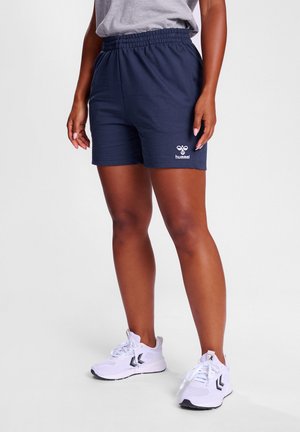 Marineblauwe sportshorts met een elastiche tailleband, voorzien van een wit logo. Gecombineerd met witte sneakers en een grijs T-shirt.