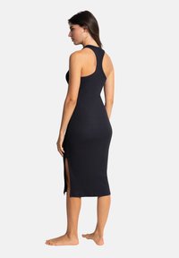 Robe noire à côtes, sans manches, longueur mi-mollet et fentes sur les côtés. Silhouette ajustée qui met en valeur le corps. Design minimaliste.