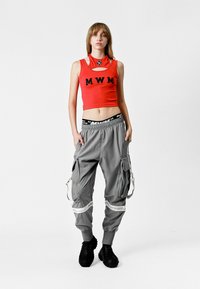 Top corto rojo con letras "MWM", combinado con pantalones cargo grises con bolsillos y zapatos negros de estilo senderismo.