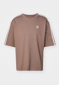 Brun Adidas T-shirt med vita ränder längs ärmarna och liten vit Adidas trefoil-logga på vänster bröst.