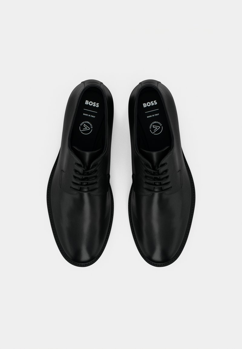 Para czarnych skórzanych butów formalnych z wiązaniami, marki "BOSS", wyeksponowana obok siebie na białym tle.
