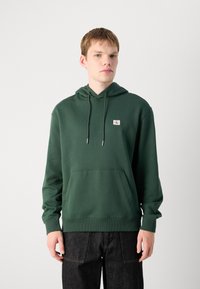 Felpa verde con cappuccio regolabile, tasca a canguro frontale, polsini e orlo a coste. Piccola patch con logo sul petto. Materiale in cotone liscio.