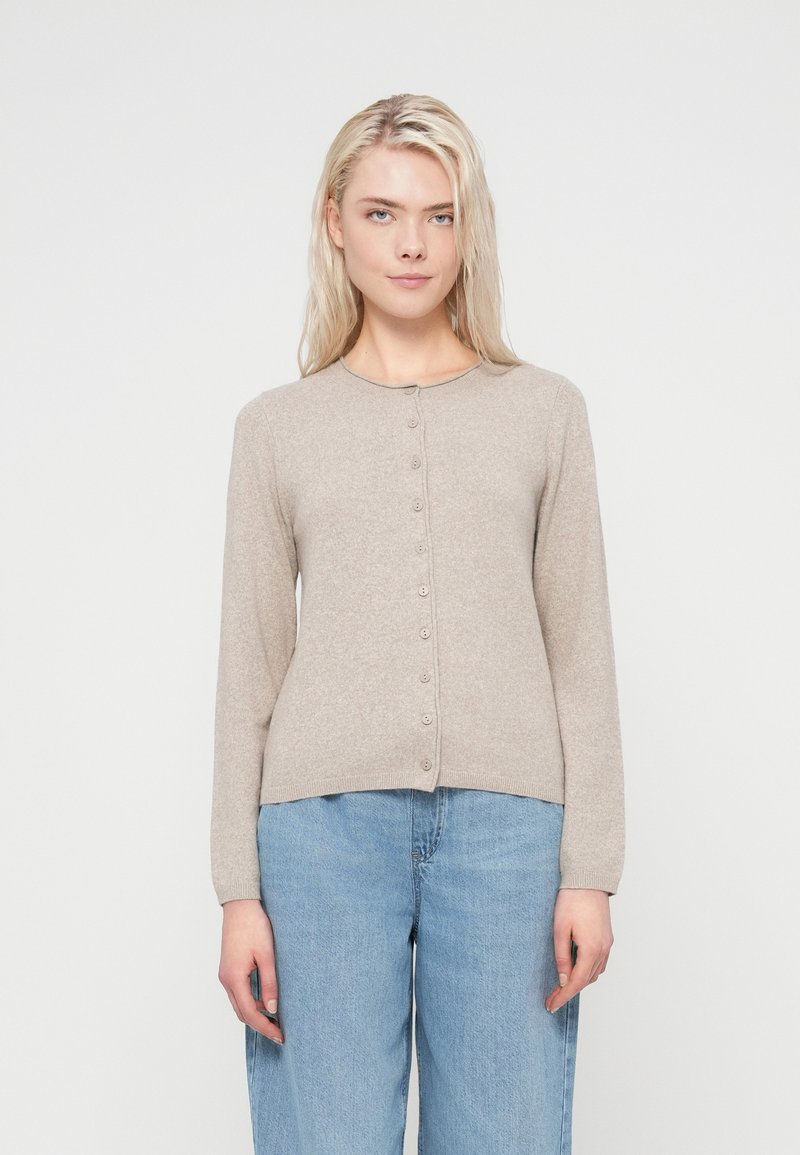 Light beige cardigan with a round neckline, long sleeves, and a button front. Soft texture, fitted cut, paired with loose blue jeans.
