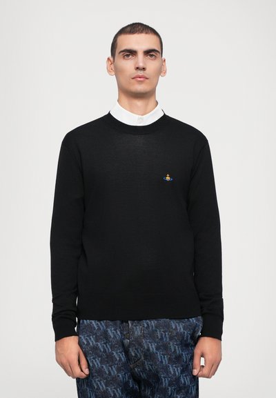 Black knit sweater with a round neckline, long sleeves, and a small embroidered logo on the chest. Worn over a white collared shirt.