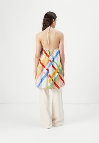 Haut à nouer coloré avec une coupe ample, présentant un motif géométrique orange, bleu, vert et jaune, associé à un pantalon large couleur crème.