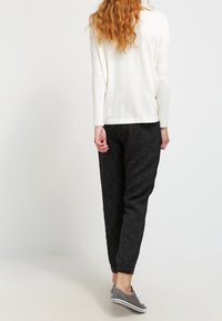 Witte lange mouwen top, zwarte geprinte joggingbroek met elastische manchetten en grijze sneakers, gezien vanachter. Glad textuur, ontspannen pasvorm.