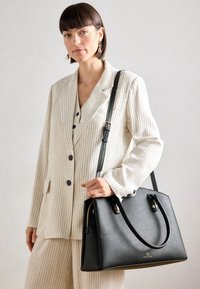 Black leather handbag with two handles and a detachable strap. Features a zip closure and gold logo detail on the front.