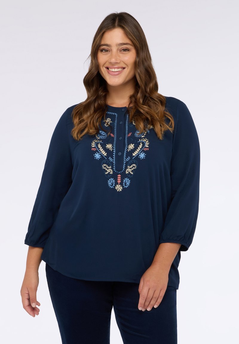 Marineblauwe blouse met driekwartmouwen, voorzien van veelkleurige bloemenborduursels langs de halslijn en de knoopsluiting. Zachte stoftextuur.