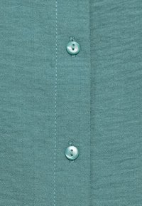 Κοντομάνικο πουκάμισο σε ανοιχτό γαλάζιο χρώμα, κοντινή λήψη, με υφή ύφασμα, δύο στρογγυλά κουμπιά και ορατές γραμμές ραφής.