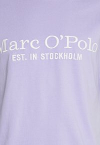 T-shirt lilas clair en tissu doux avec 'Marc O'Polo' et 'EST. À STOCKHOLM' brodés en blanc. Design simple sans motifs.