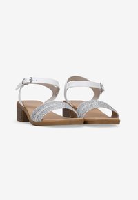 Sandales blanches à lanières avec des détails en paillettes argentées sur le devant, un talon bloc marron et une bride de cheville ajustable.