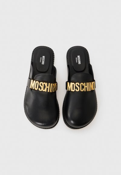 Svarta slip-on sandaler med guld MOSCHINO-tryck över remmarna och MOSCHINO Milano tryckt på innersulorna.