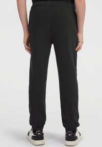 Zwarte sweatpants met een elastische tailleband en boorden, met een zachte stoffen textuur. G gedragen met zwart-witte sneakers.