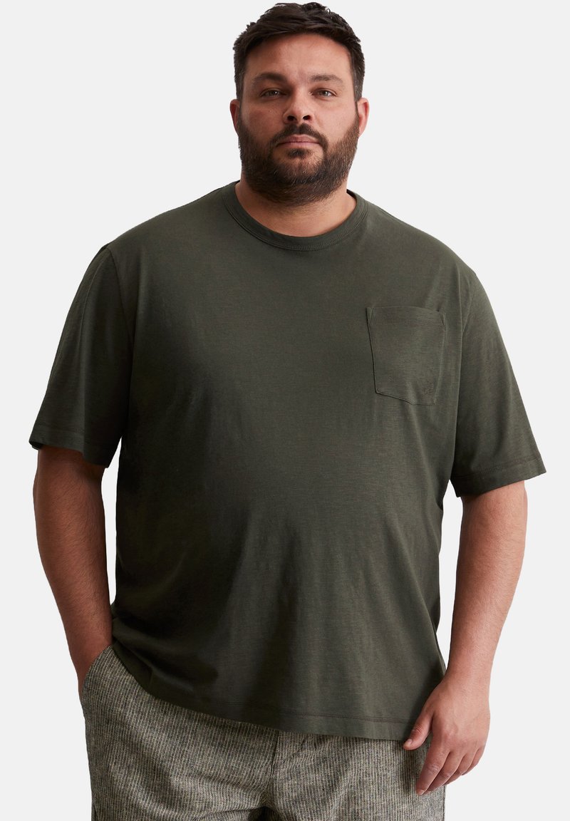 T-shirt olive à manches courtes en tissu doux, avec une poche poitrine et une coupe décontractée. Pantalons à motifs texturés gris clair.