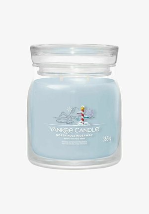 Lyseblå Yankee Candle med North Pole Hideaway duft, med et snedækket landskab og et stribet North Pole-skilt på forsiden.