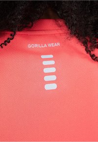 Koraalkleurig sportshirt van textuurstof; heeft een witte "GORILLA WEAR" logo en 4 horizontale streepaccenten op de achterkant.