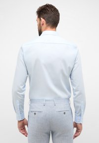Lichtblauw overhemd met lange mouwen en geknoopte manchetten, gecombineerd met lichtblauwe getextureerde broeken met twee achterzakken.