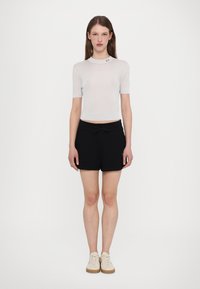 Ljust grå ribbad t-shirt med kort ärm och rundad halsringning, kombinerat med svarta shorts med snörning. Modellen har på sig beiga sneakers.
