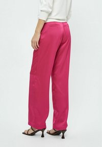 Fuchsia wide-leg pants in satin fabric. Features back pockets, smooth texture, and hemmed bottoms. Paired with heeled sandals.