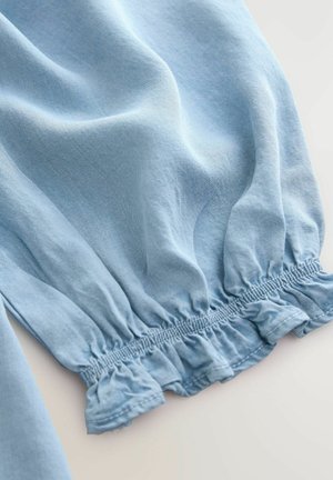 Tessuto di cotone azzurro chiaro con orlo arricciato e a balze. La texture morbida, la finitura liscia e una leggera lucentezza sono visibili nelle pieghe.