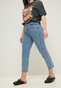 Light blue denim jeans with pearl embellishments, featuring a straight leg design and mid-rise waist. Paired with a graphic t-shirt and black clogs.