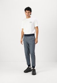 Marineblaue Jogginghose mit geometrischem Muster, elastischem Bund, seitlichen Streifen und gerippten Bündchen, kombiniert mit einem weißen Rundhalsausschnitt-T-Shirt.