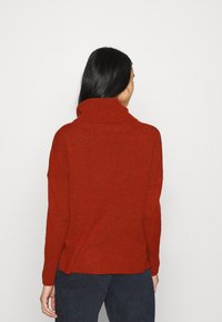 Maglione rosso lavorato a maglia con colletto alto a coste, vestibilità ampia e spacchi laterali all'orlo. Tessuto morbido con un sottile motivo screziato.