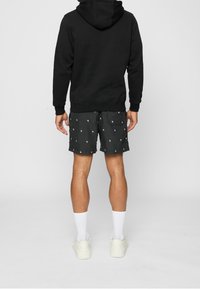 Felpa nera con coulisse, indossata sopra pantaloncini grigi con motivo bianco. Calzini bianchi alti abbinati a sneakers bianche.