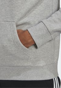 Sudadera gris con un acabado texturizado, bolsillo canguro y puños de canalé. Presenta un corte relajado con una cinturilla en un tono gris similar.