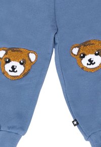 Blauwe stoffen broek met gestructureerde bruine en witte teddybeer gezichten op elke knie en ribbelboorden bij de enkels.