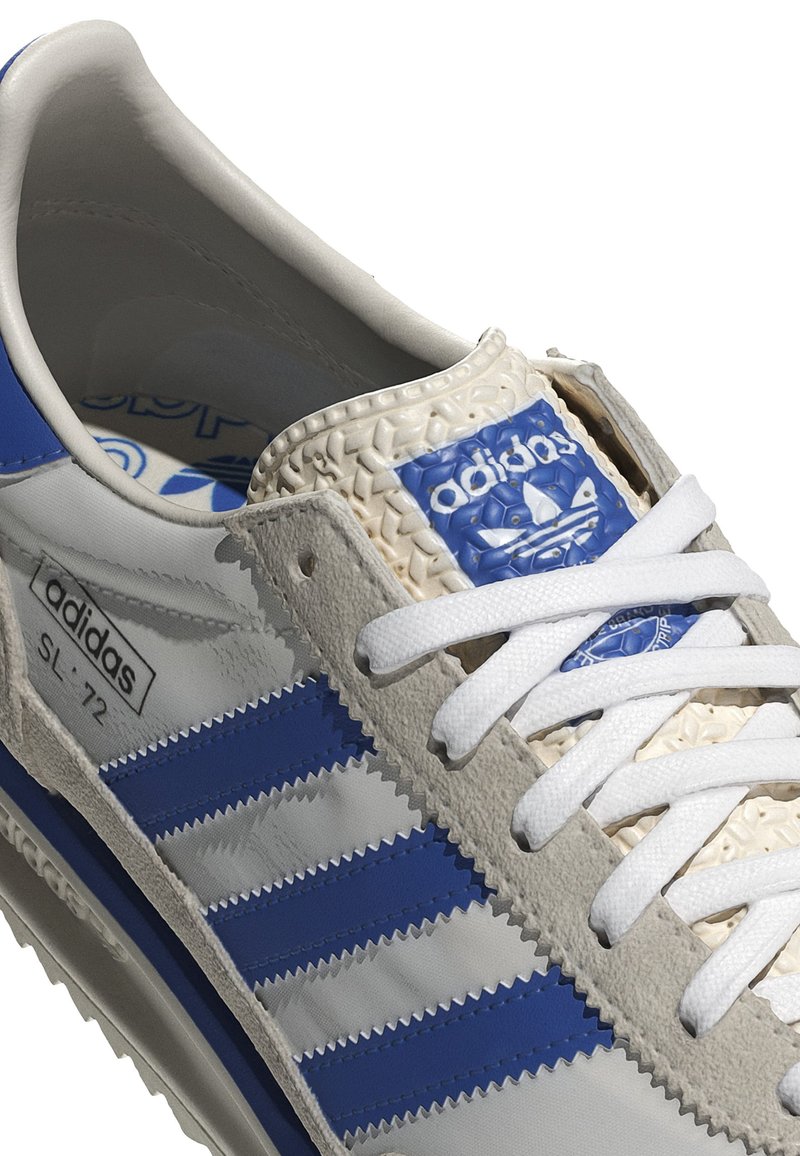 Sneakers Adidas SL-72 z szaro-niebieską skórzaną cholewką, trzema niebieskimi paskami, teksturowanym kremowym językiem i białymi sznurowadłami.