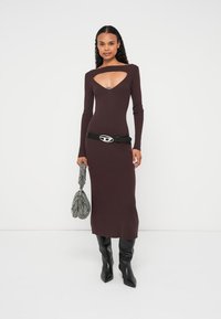 Adīta kastaņu krāsas kleita ar V veida izgriezumu, garām piedurknēm un piegulošu piegriezumu. Kombinēta ar melniem zābakiem līdz ceļiem un teksturētu pelēku somiņu.