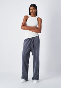 Canotta bianca senza maniche e pantaloni della tuta grigi con coulisse. I pantaloni hanno una vestibilità larga con una trama morbida e un motivo sottile. Scarpe bianche.