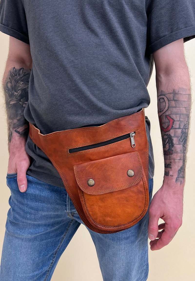 Tan leather fanny pack with a smooth texture, featuring a zippered pocket and a front snap-flap pocket. Worn around the waist.