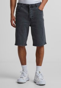 Dunkelgraue Denim-Shorts mit lockerer Passform, normalen Taschen und umgeschlagenen Säumen, kombiniert mit weißen Sneakern und Socken.