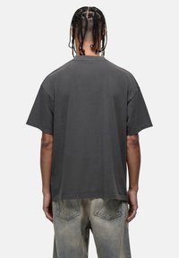 Szary, oversize t-shirt z krótkimi rękawami, okrągłym dekoltem i luźnym krojem, wykonany z bawełny o gładkiej fakturze. Brak widocznych logo lub wzorów.